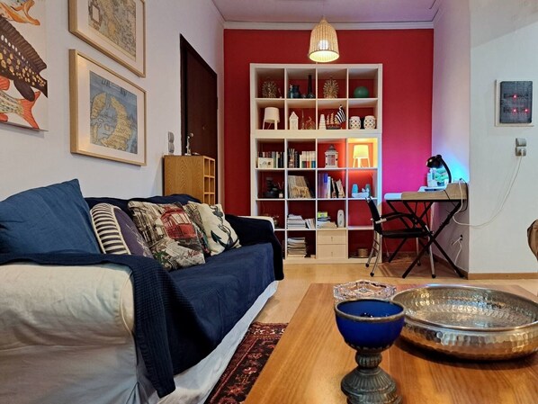 Una sala de estar acogedora con un sofá azul, una mesa de centro de madera y una estantería llena de objetos diversos.