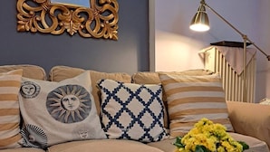 Ein gemütliches Wohnzimmer mit einer Couch, verziert mit gemusterten Kissen, einem Dekospiegel und einer Vase mit gelben Blumen auf einem Tablett.