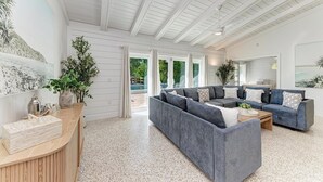 Amplia sala de estar con un sofá seccional gris grande, una mesa de centro de madera y un techo blanco con vigas a la vista.