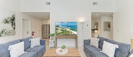 A modern living room with two grey sofas, a wooden coffee table, and a large flat-screen TV.