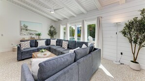 Amplio salón con un sofá seccional gris, una mesa de centro y un ventanal con vistas a una piscina.