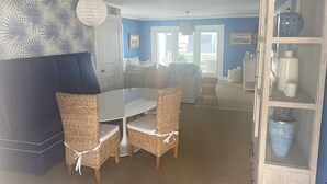 A dining area with a round table and wicker chairs, a blue accent wall, and a decorative shelf with vases. - 4 bedroom, 2 bath home with 3 porches, & steps from the beach in Atlantic Beach (Atlantic Beach)
