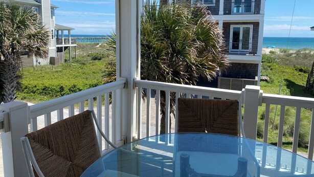 A glass table with two wicker chairs on a balcony overlooking a beach and a two-story house. - 4 bedroom, 2 bath home with 3 porches, & steps from the beach in Atlantic Beach (Atlantic Beach)