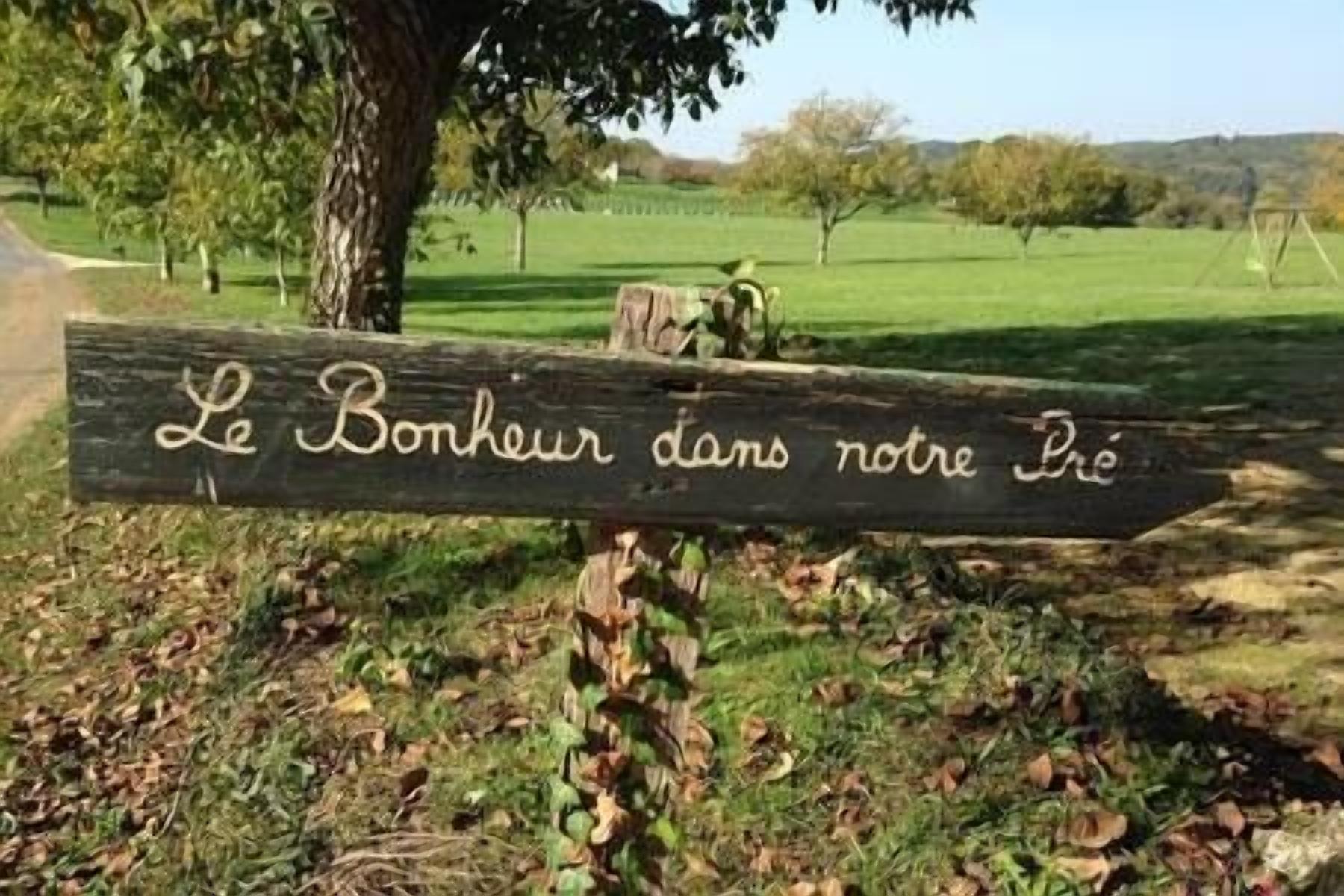 Une enseigne en bois portant l’inscription « Le Bonheur dans notre Prie », en caractères cursifs.