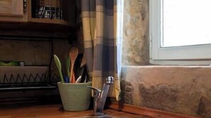 A kitchen sink with a faucet, a green bowl with utensils, and a window with a view of the outside.