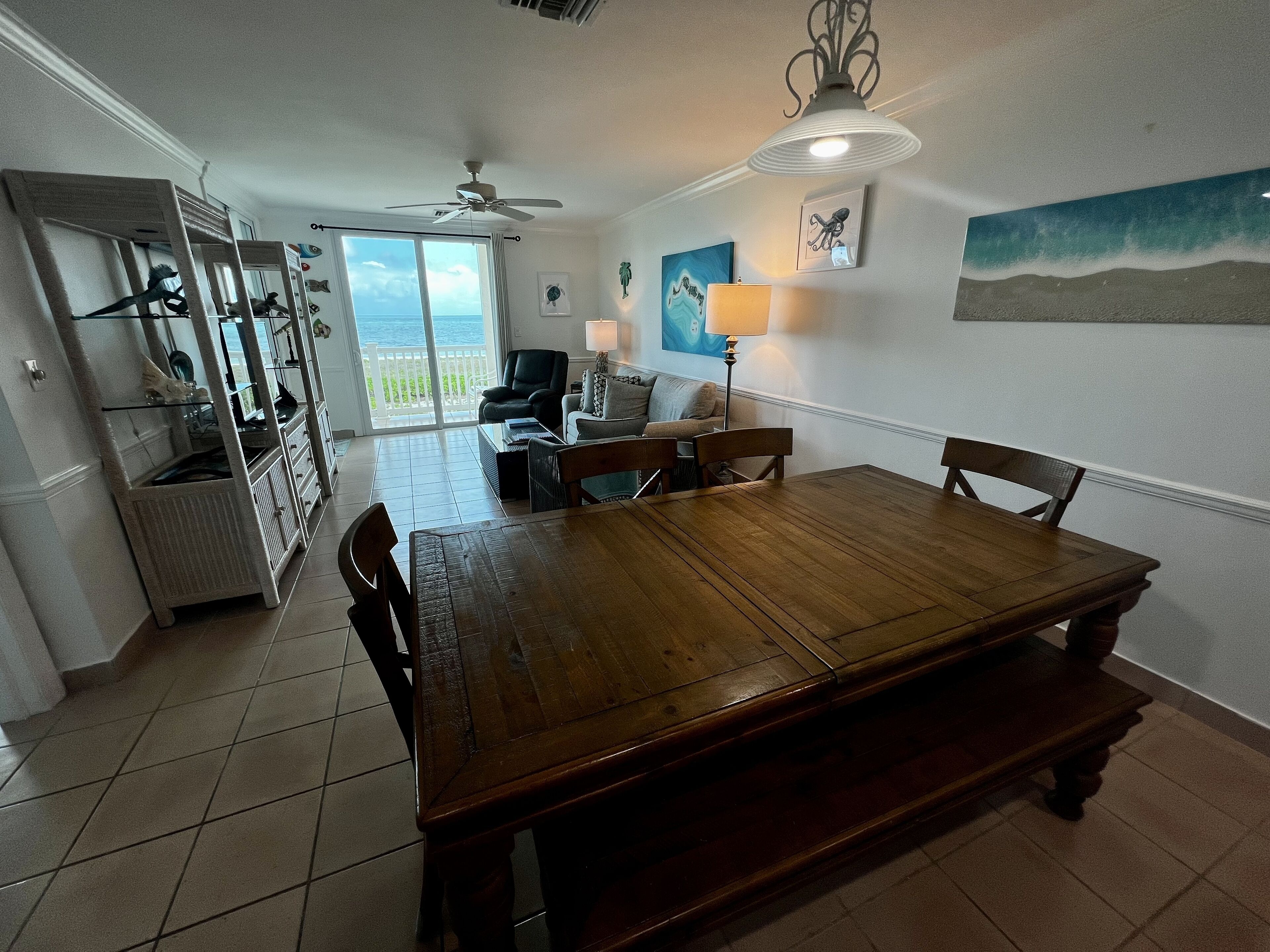Un comedor amplio con una mesa y sillas de madera, un ventilador de techo y vistas al exterior a través de un ventanal.