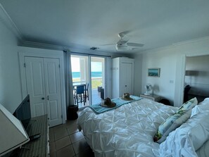 Habitación de hotel con cama, escritorio, silla, ventilador y vista a la playa.