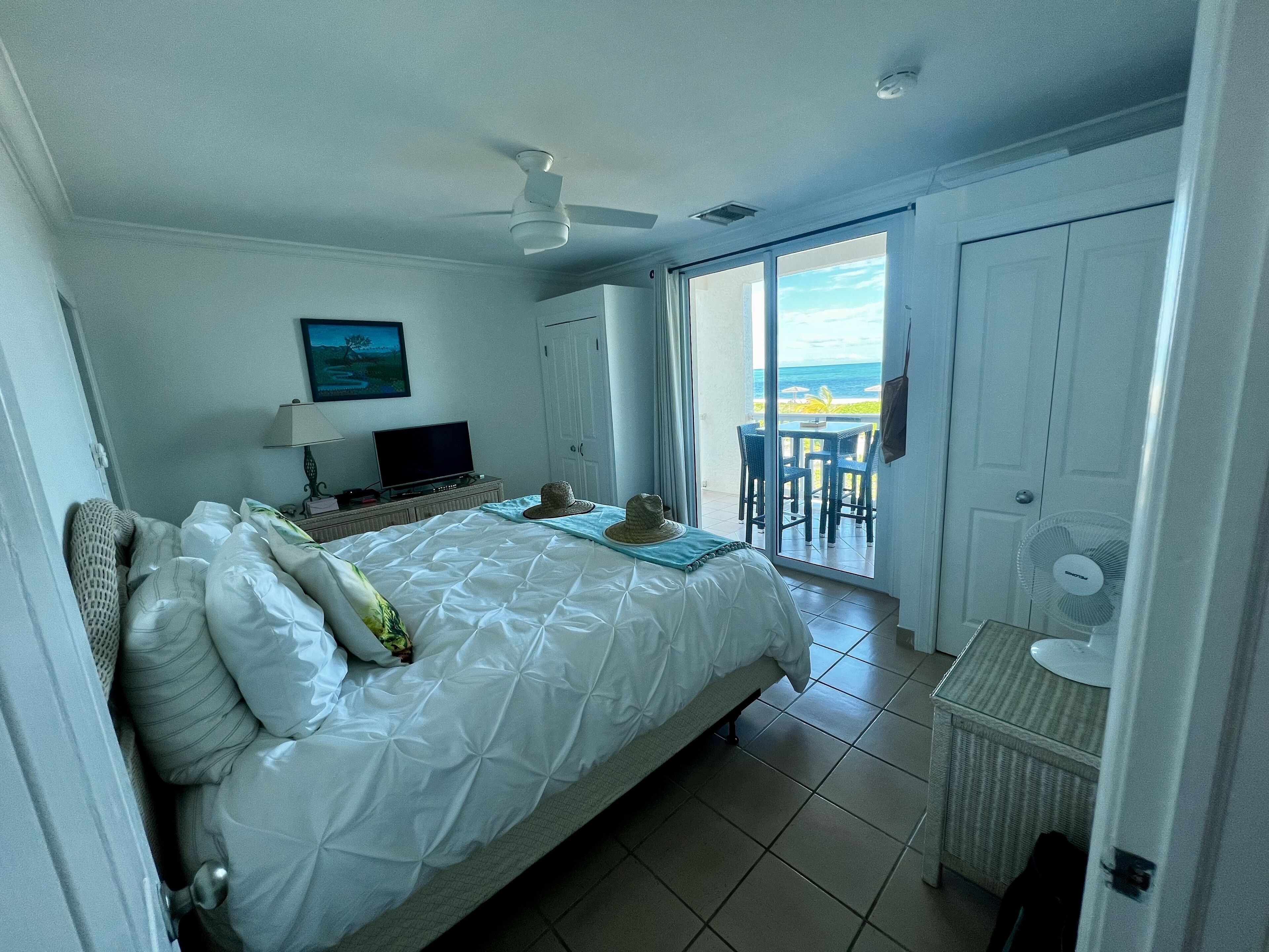 Une chambre d’hôtel équipée d’un lit, d’une télévision, d’un ventilateur et offrant une vue sur l’océan grâce à une porte coulissante.
