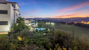 Ein modernes Gebäude mit Pool, umgeben von üppiger Vegetation und Blick auf eine ferne Stadt im Abenddämmerung.