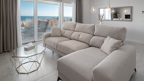 En moderne stue med en beige hjørnesofa, et sofabord i glas og havudsigt gennem store vinduer.