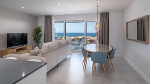 En moderne stue med fjernsyn, sofa, spisebord og stole. Der er et stort vindue med havudsigt.