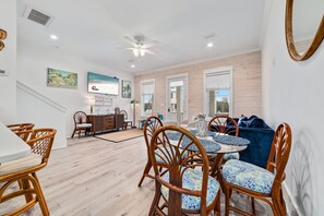 Un vaste espace de vie comprenant une table à manger, des chaises en osier, un canapé bleu et un ventilateur de plafond.