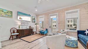 A spacious living room with a wooden floor, a white sofa, a blue armchair, and a TV mounted on the wall.