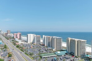 A coastal cityscape with high-rise buildings, a beach, and a parking lot.