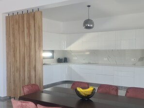 A modern kitchen with white cabinets, a marble backsplash, and a dining area with a dark wooden table and red chairs.