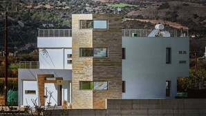 A modern multi-story building with a flat roof, large windows, and a mix of stone and concrete materials. - Modern Luxury Villa near Lachi (Prodromi)
