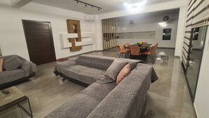 A modern living room with a grey sectional sofa, a small table, and a dining area with orange chairs and a black table. - Modern Luxury Villa near Lachi (Prodromi)