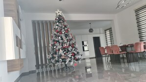 A modern living room with a Christmas tree, a dining area with pink chairs, and a kitchen with a built-in oven. - Modern Luxury Villa near Lachi (Prodromi)