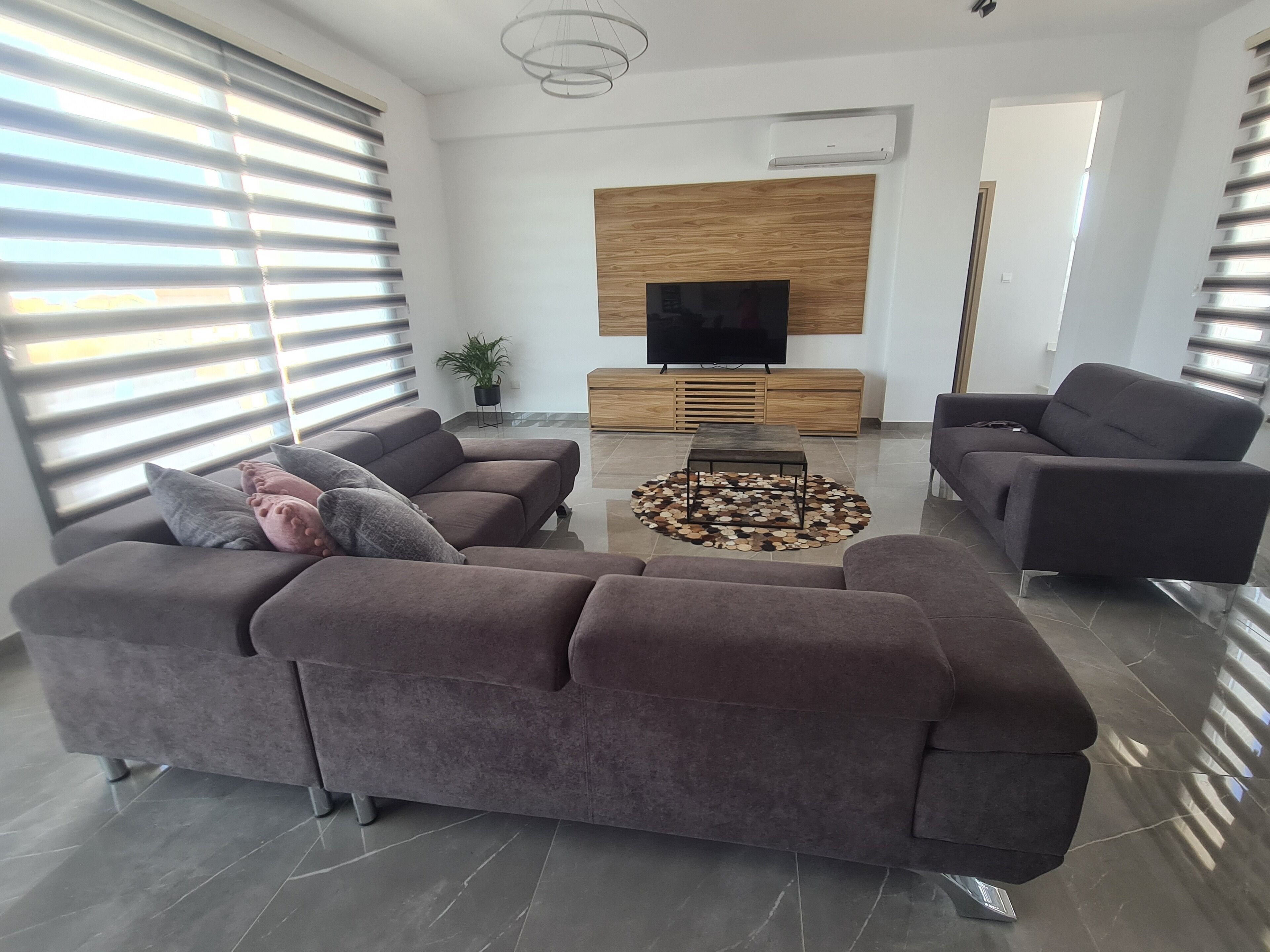 Uma sala de estar moderna com um sofá seccional, uma mesa de centro e uma televisão de tela plana fixada em um painel de madeira.
