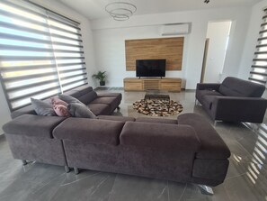 Un salon moderne avec un canapé d’angle, une table basse et un téléviseur à écran plat fixé sur un panneau en bois.
