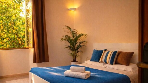 Une chambre à coucher avec un lit, une plante en pot, une fenêtre avec des rideaux et un luminaire fixé au mur.