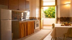 Une cuisine équipée d’une cuisinière, d’un four et de placards, une table à manger avec des chaises, et une vue sur la verdure à l’extérieur.