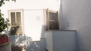 Un petit espace extérieur clos, avec un mur blanc, une fenêtre à volets et un sol en béton.