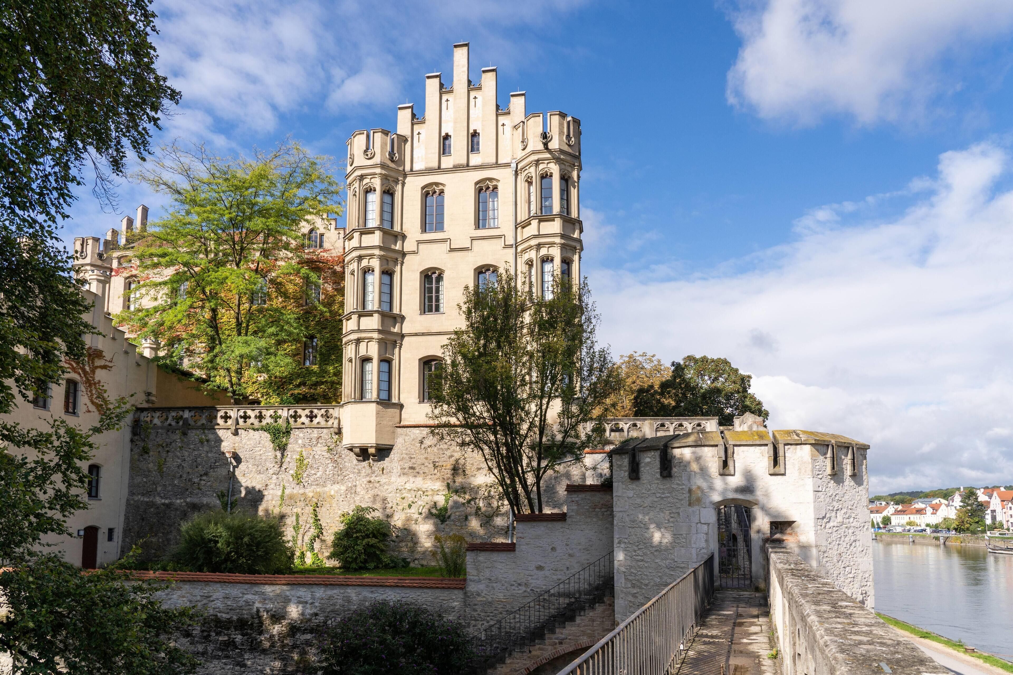 Un edificio histórico con una torre, un muro de piedra y un río al fondo.