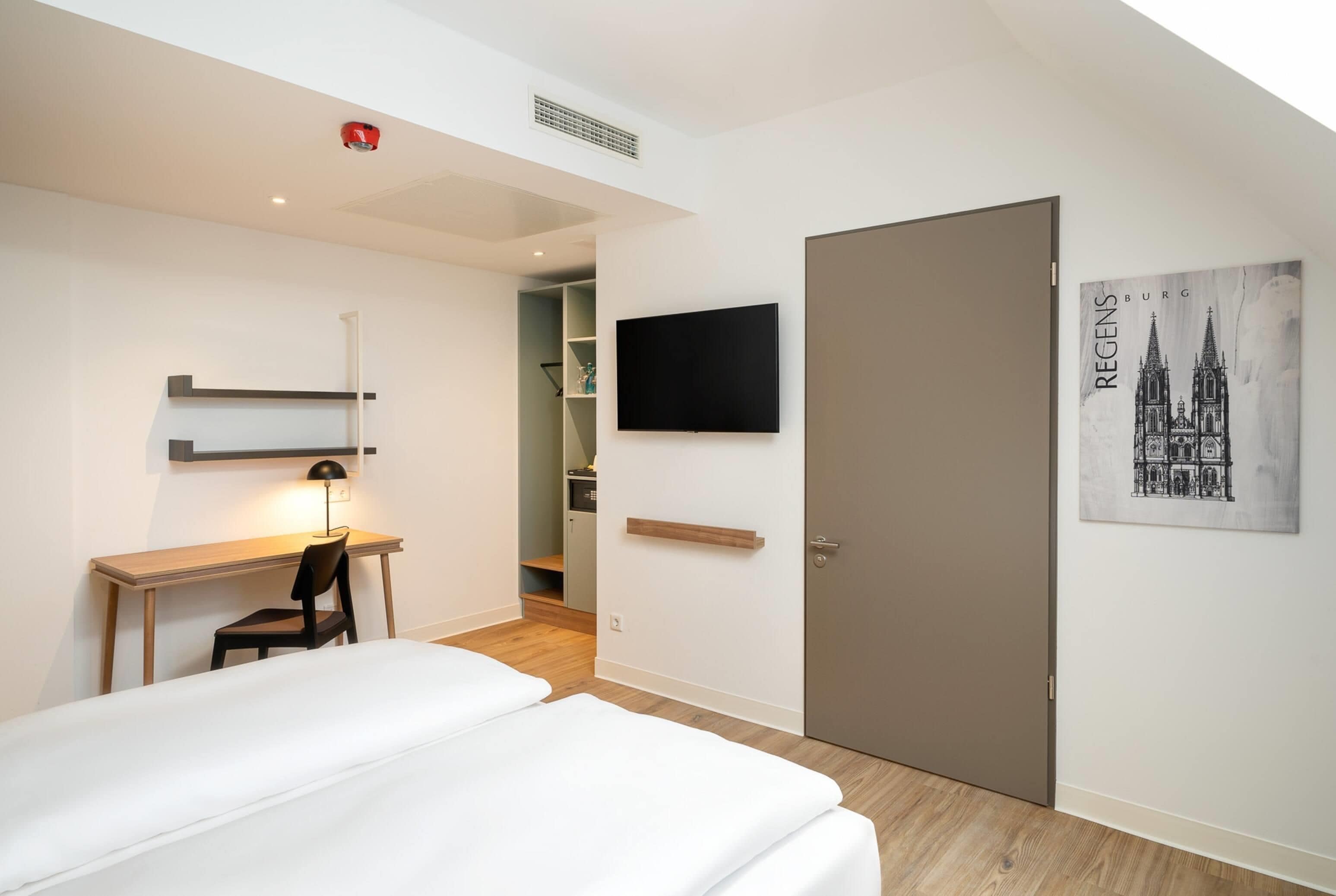 Ein Hotelzimmer mit Bett, Schreibtisch, Stuhl, Fernseher und einer Tür.