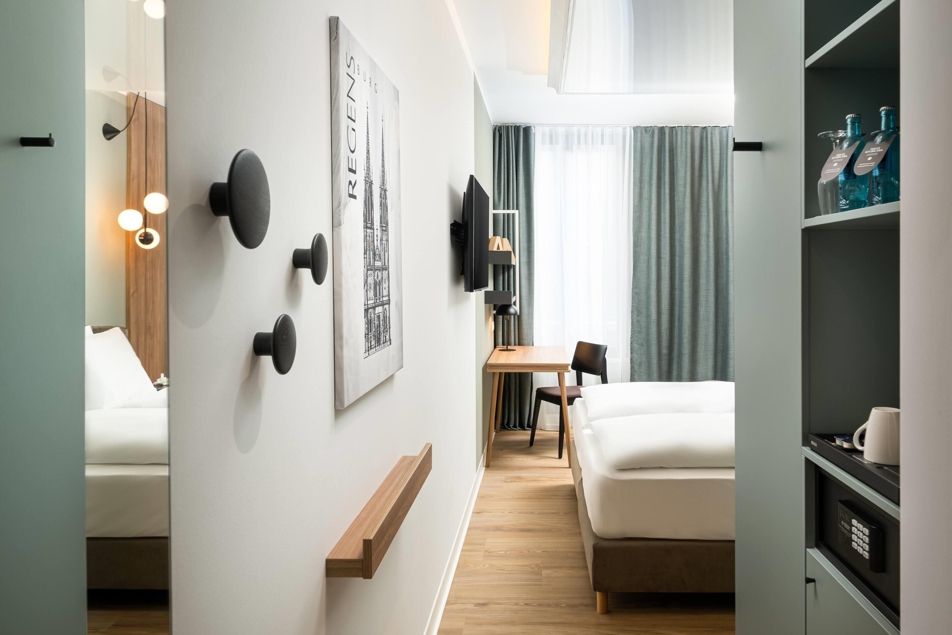 Una habitación de hotel moderna con cama, escritorio, silla, televisor y un minibar.
