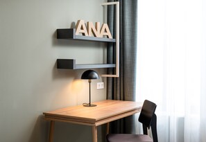 A modern room with a wooden desk, a black lamp, and a chair. There are shelves with the letters "ANA" on them. - elaya hotel regensburg city center, Trademark by Wyndham (Regensburg)