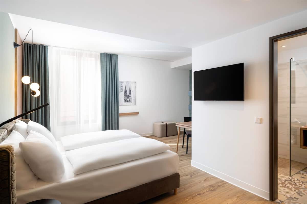 A modern hotel room with a large bed, a flat-screen TV mounted on the wall, a desk, and a chair.