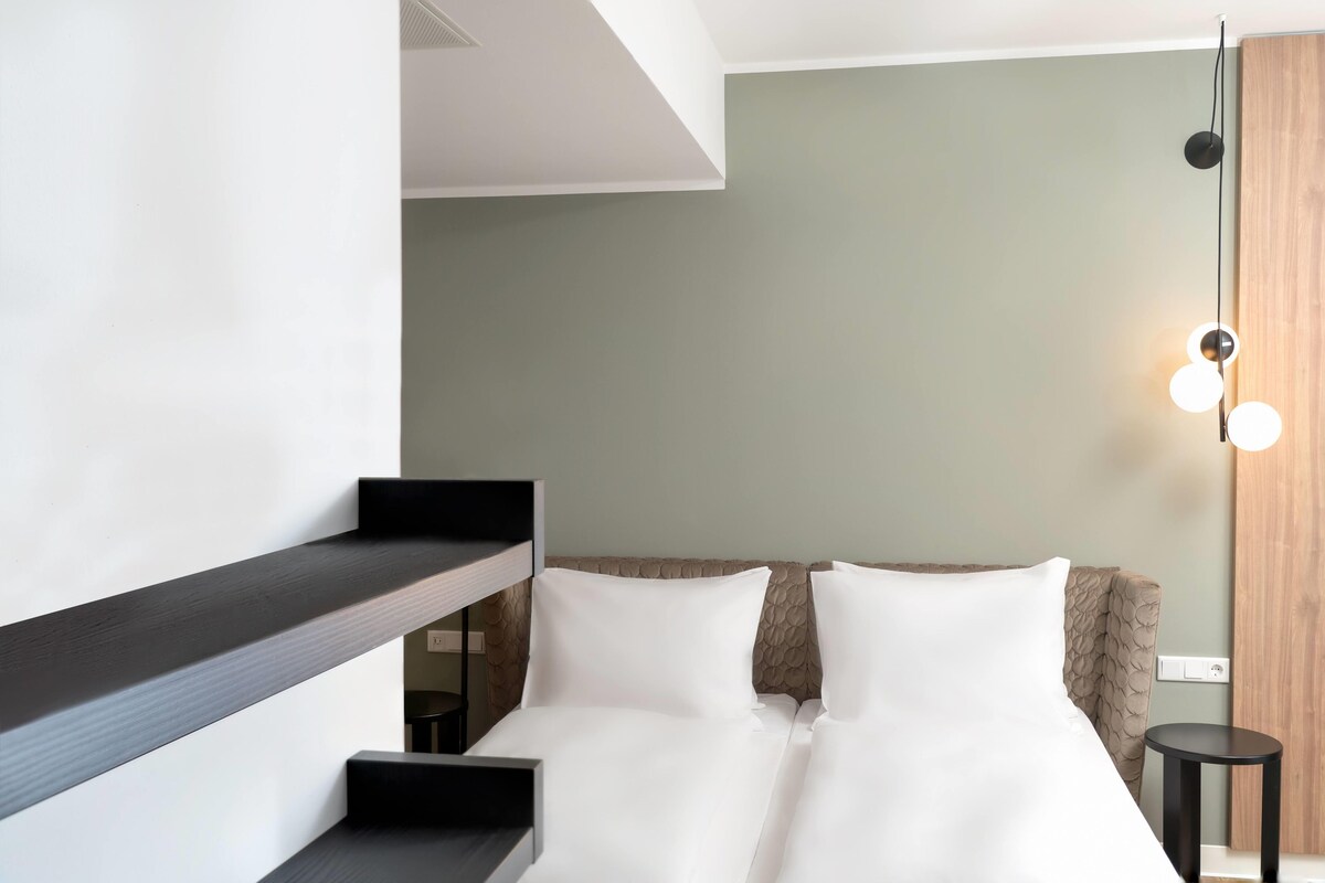 A modern hotel room with a bunk bed, a small desk, and a bedside table.