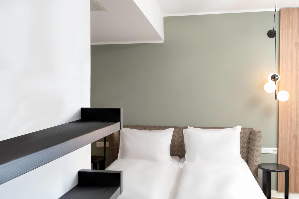 A modern hotel room with a bunk bed, a small desk, and a bedside table.