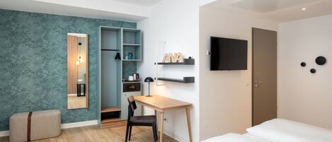 A modern hotel room with a wooden desk, a chair, a bed, a wardrobe, a TV, and a shelf with a nameplate.