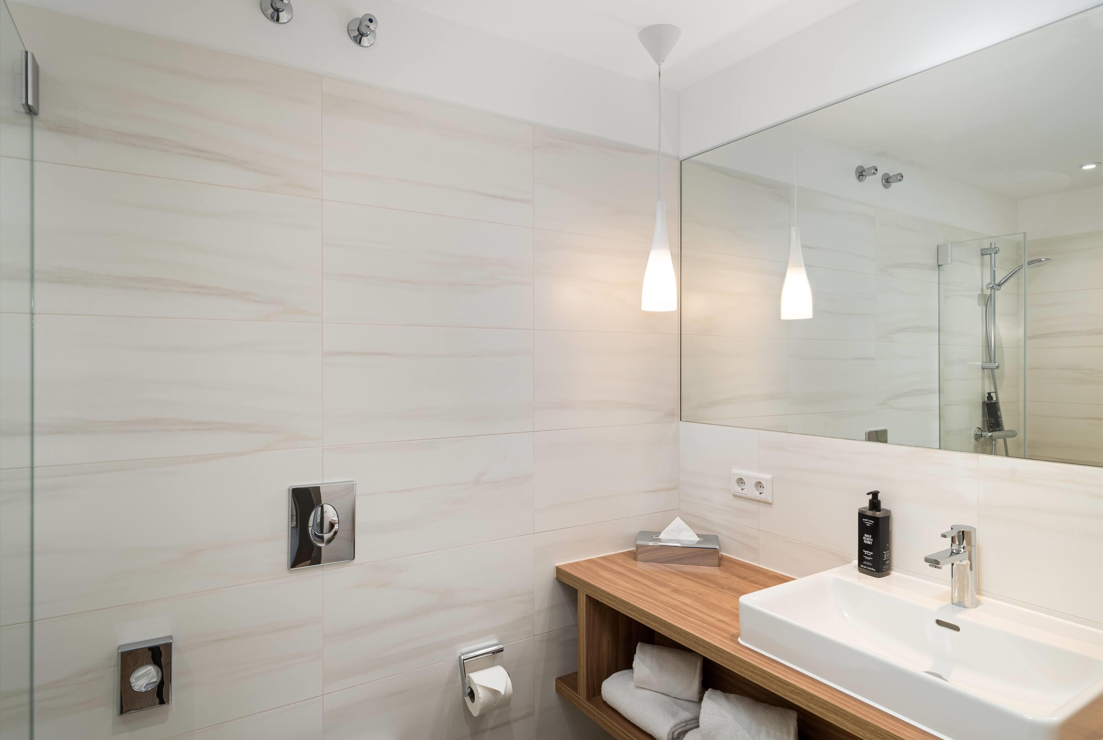 A modern bathroom with a large mirror, a wooden vanity, a white sink, and a glass shower enclosure.