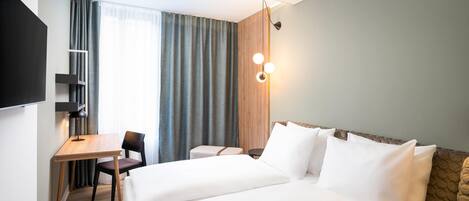 A hotel room with a bed, a desk, a chair, a TV, and a window with curtains.
