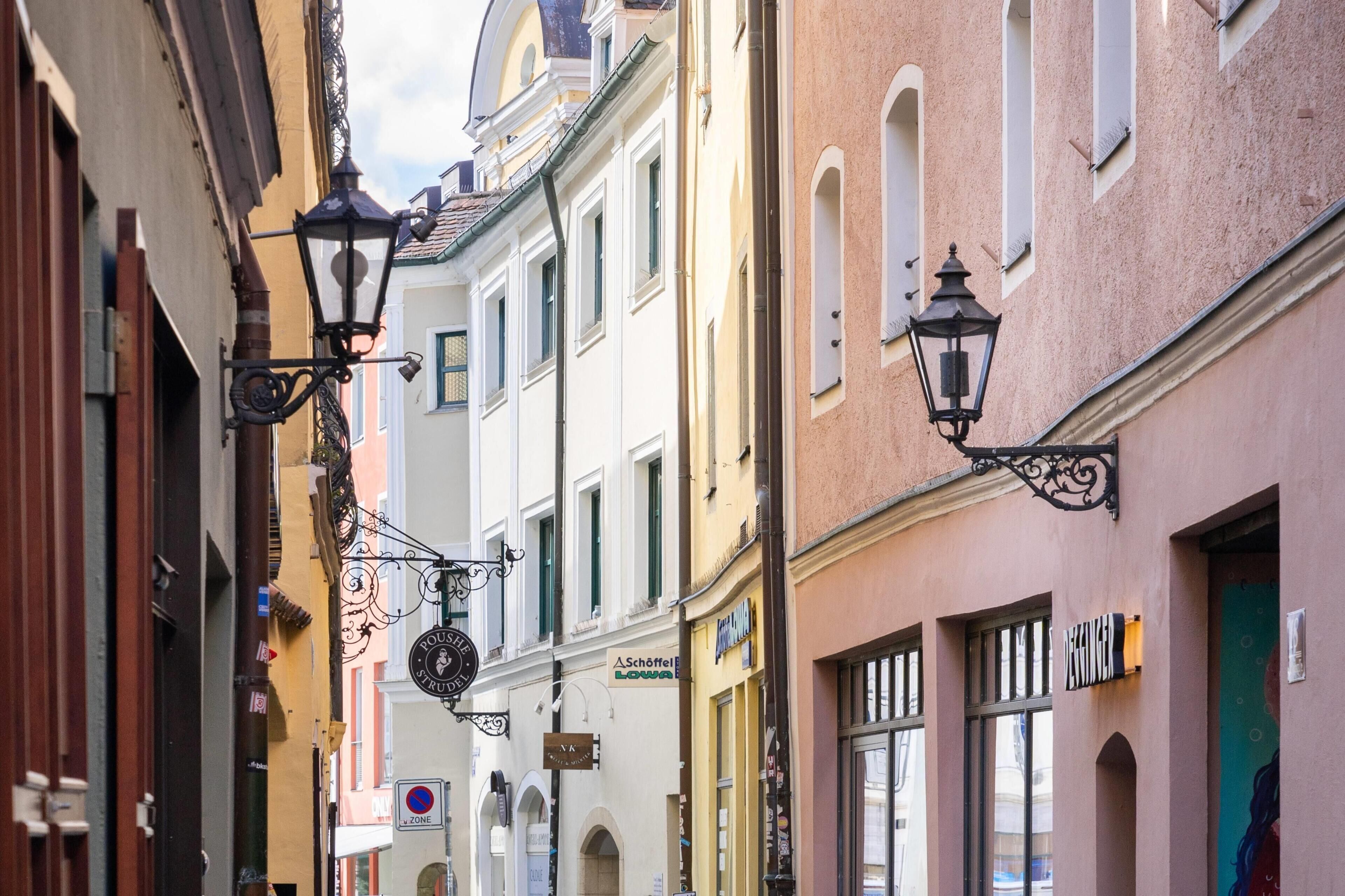 A narrow street with buildings on either side, featuring traditional architecture and hanging street lamps.