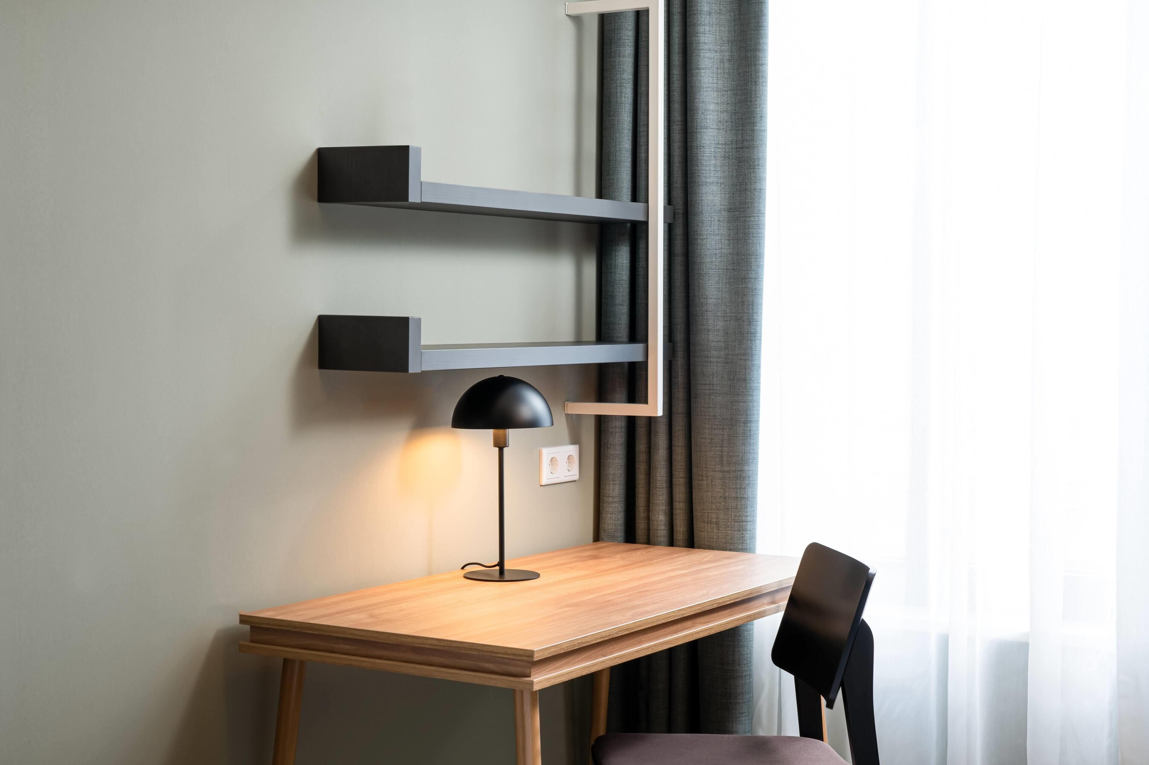 Un espacio de trabajo moderno con un escritorio de madera, una lámpara de escritorio negra y una silla.