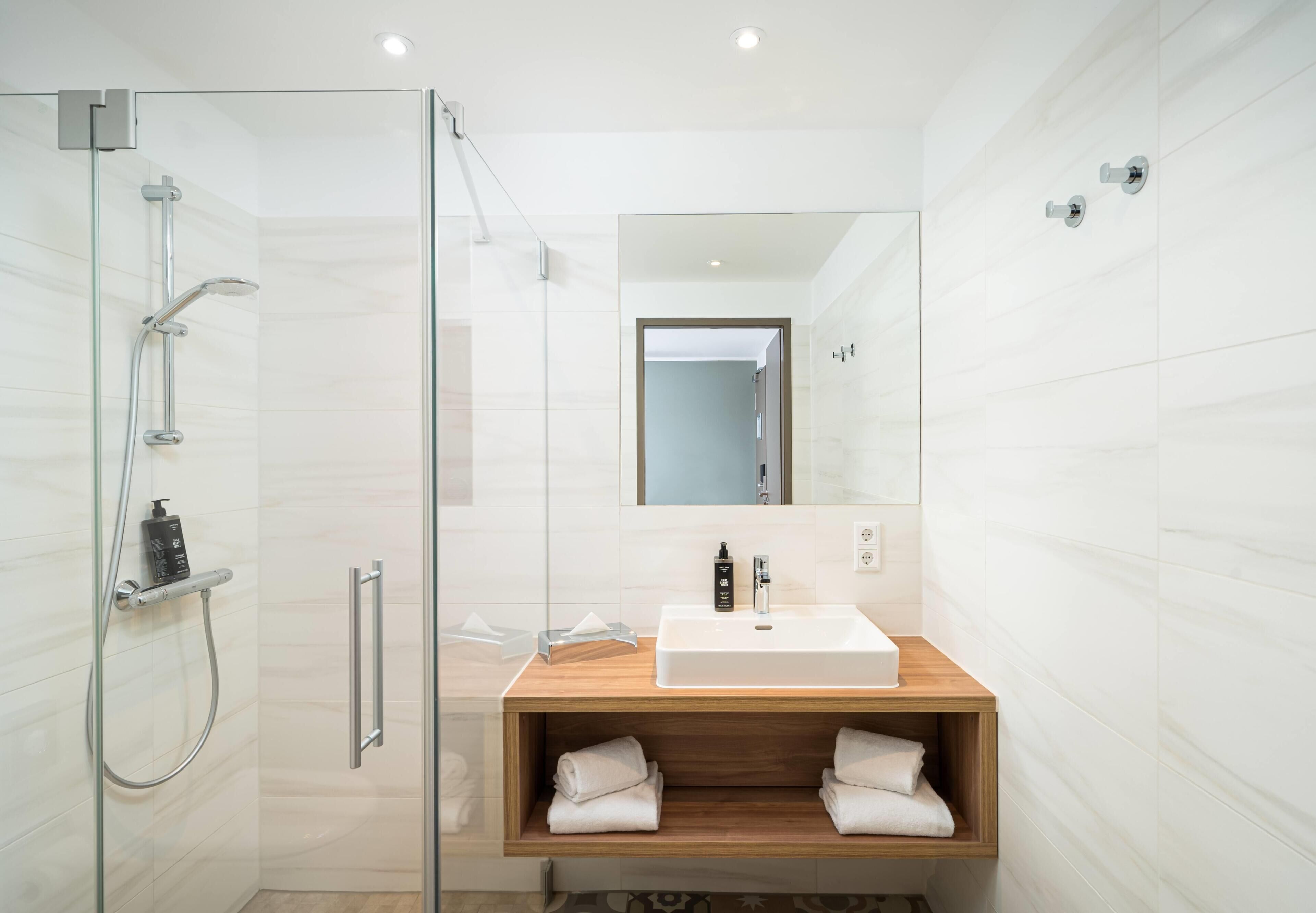 Un baño moderno con cabina de ducha de vidrio, tocador de madera con lavabo blanco y un espejo sobre el tocador.