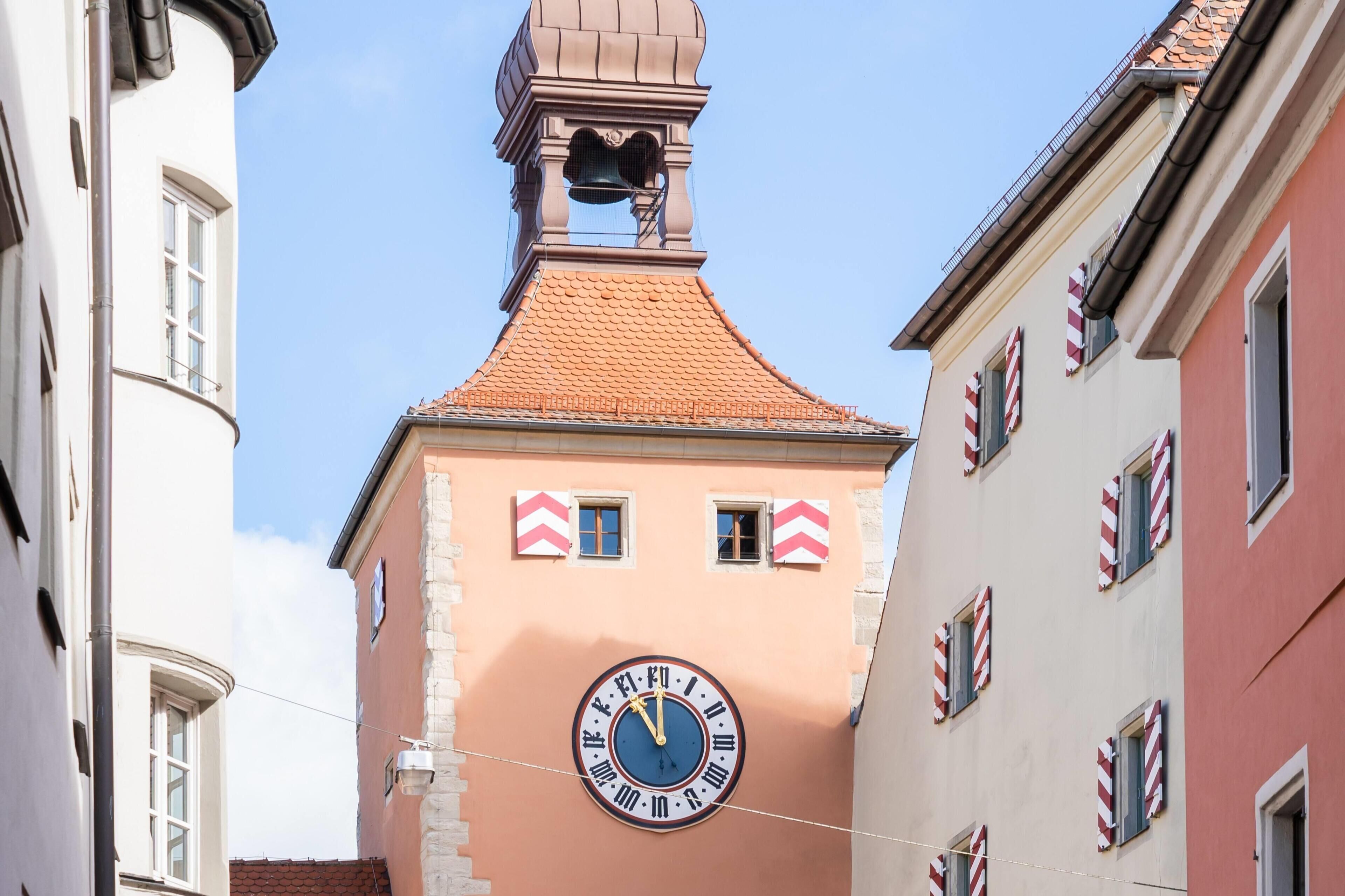 Un edificio con una torre de reloj, una campana y un toldo a rayas rojas y blancas.
