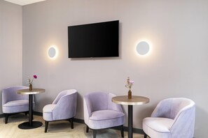 A room with a flat-screen TV mounted on the wall, two round tables with vases, and three upholstered chairs.