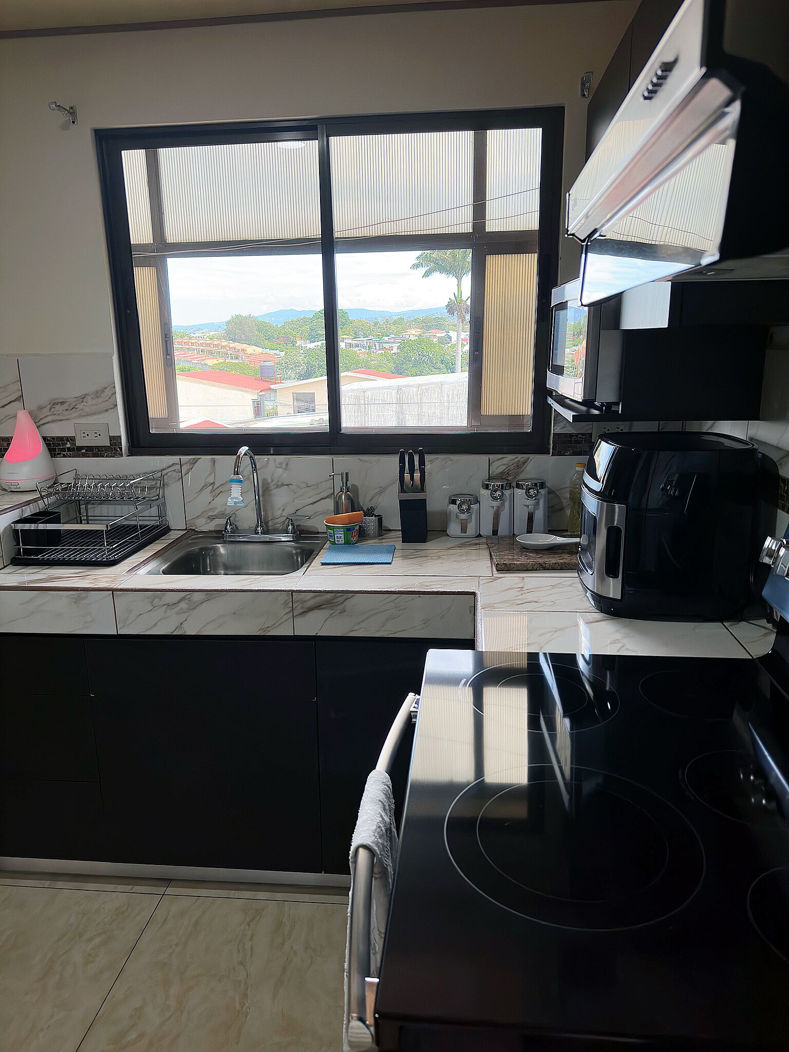 Una cocina con un ventanal grande, un lavamanos, una estufa y un microondas.