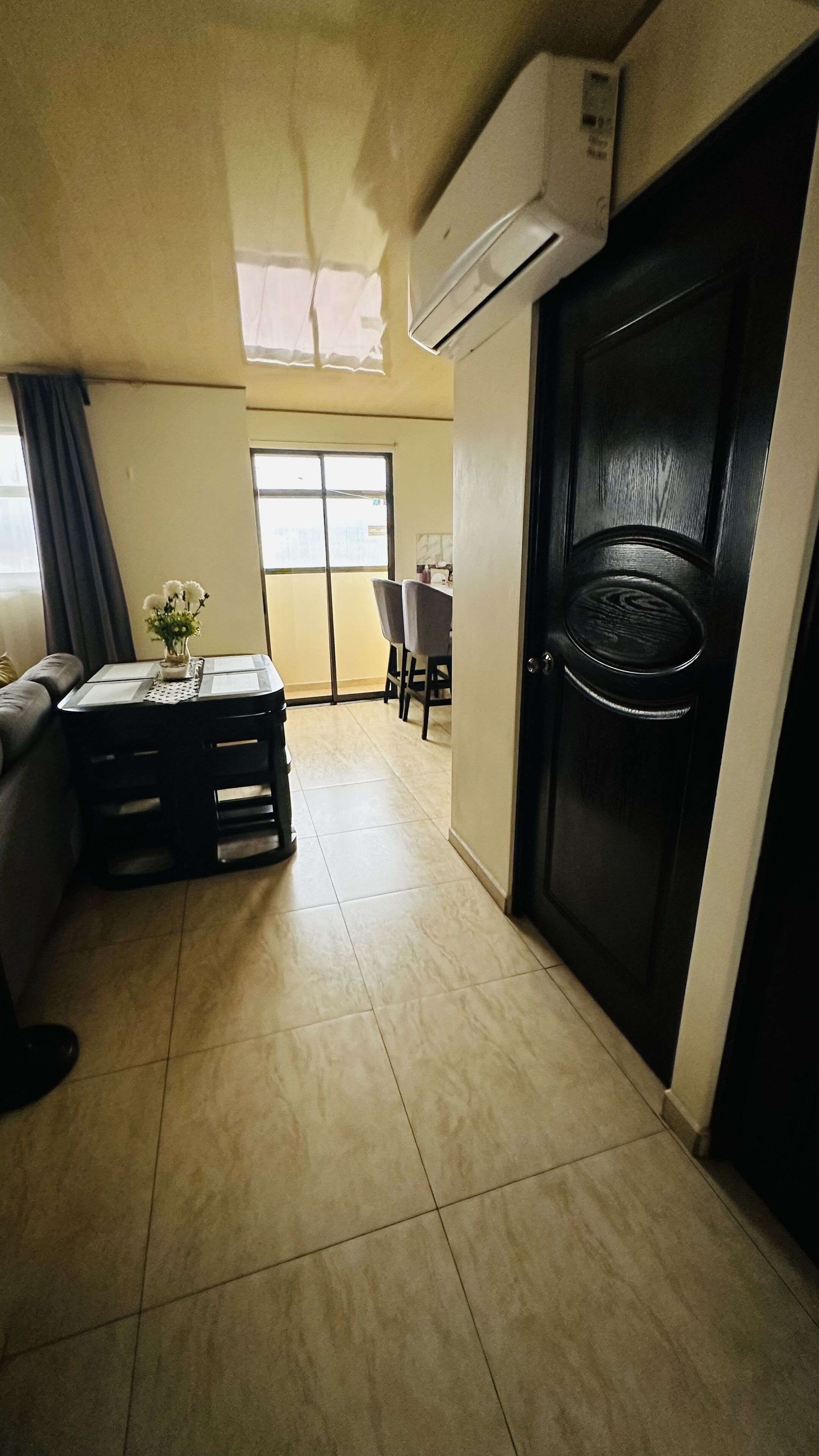 Una habitación con un sofá, una mesita con un florero, una puerta con manija y una ventana con cortinas.