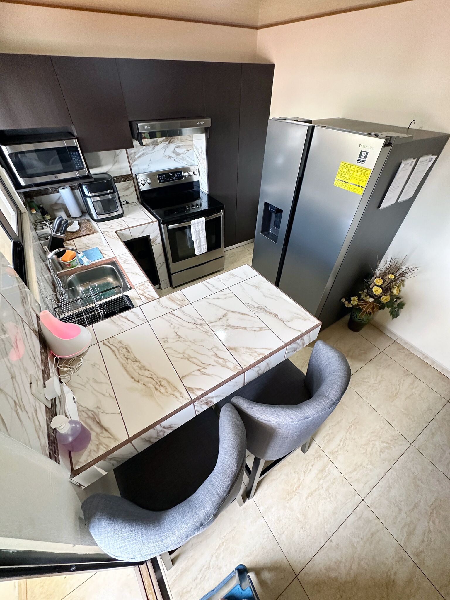 Een kleine keuken met een marmeren aanrecht, een inbouwoven, een magnetron, een koffiezetapparaat en een koelkast.