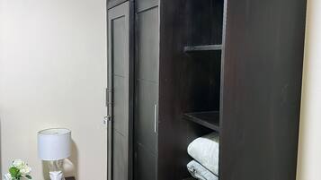 Une grande armoire en bois sombre, dotée de plusieurs portes et de tiroirs, une petite table avec une lampe et un vase de fleurs, et un sol carrelé.