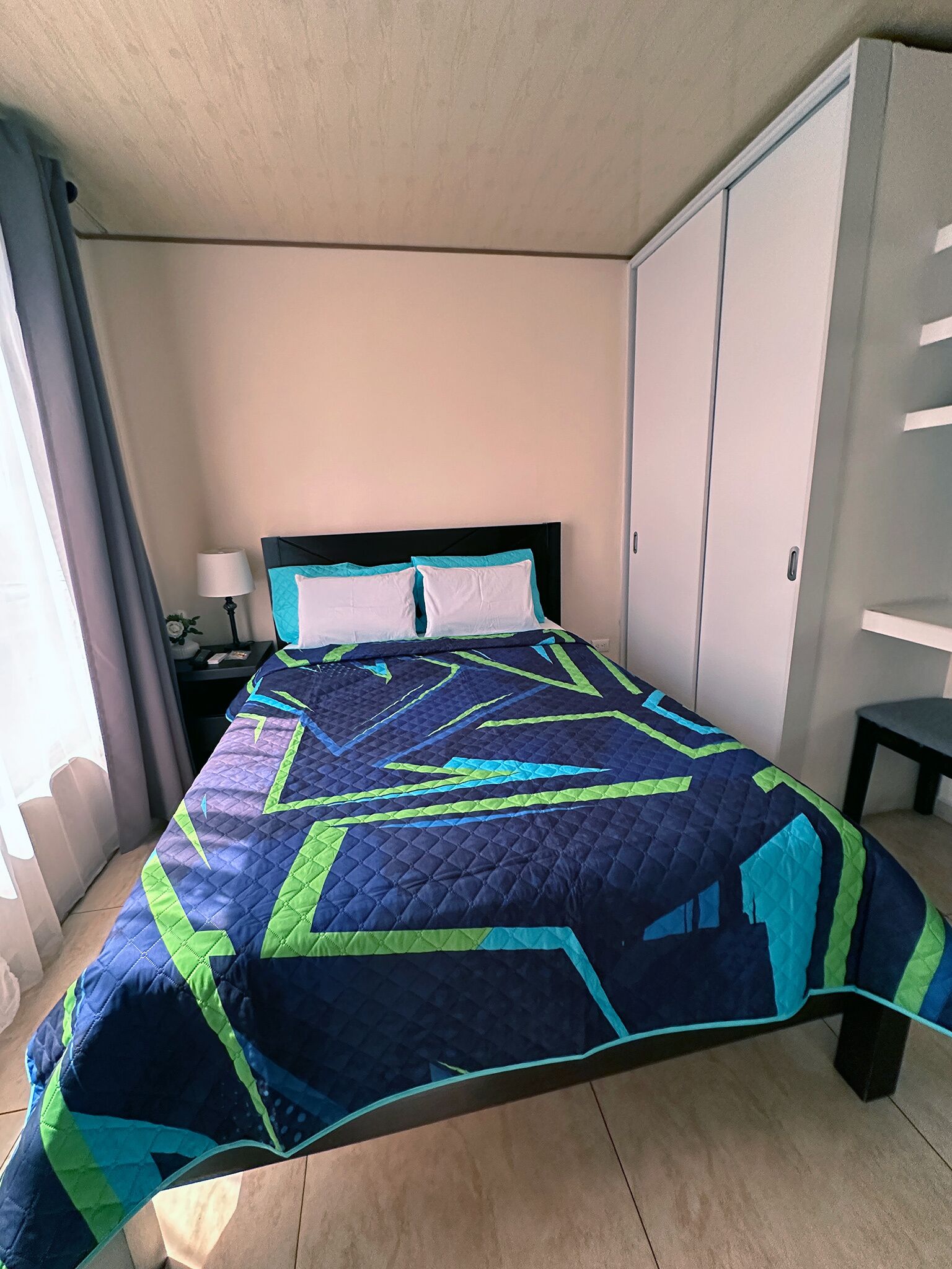 Quarto com cama, mesa de cabeceira, luminária, guarda-roupa e uma cadeira.