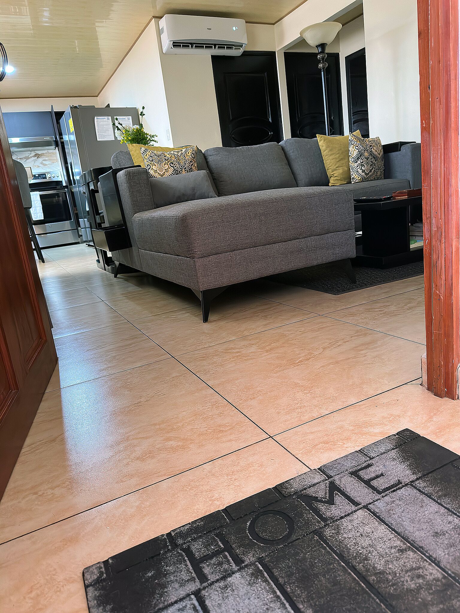 A modern living room with a grey sofa, a black coffee table, and a kitchen area in the background.