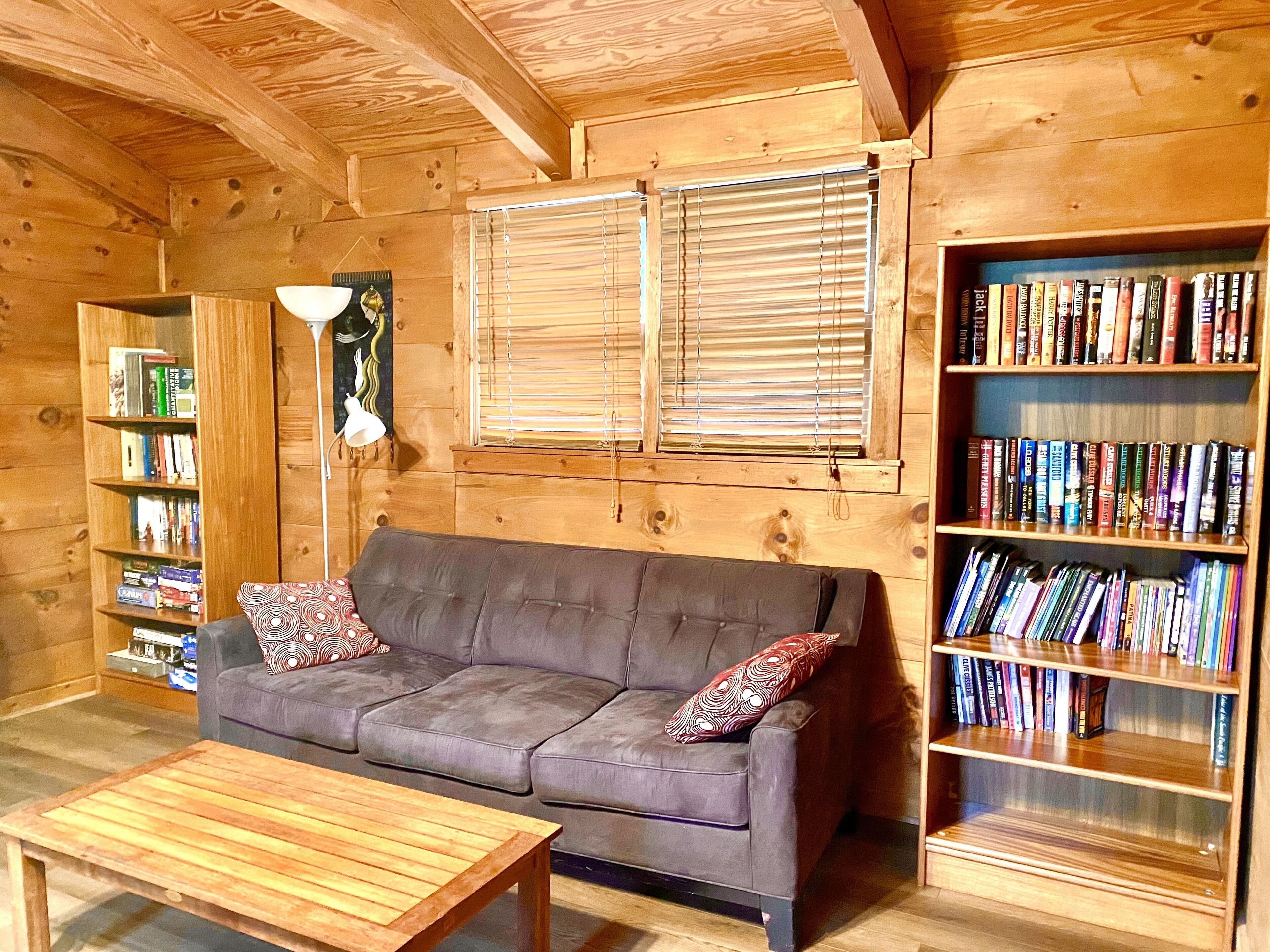 A cozy room with a grey sofa, a wooden coffee table, and a bookshelf filled with books.