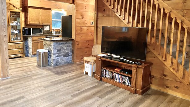Ein Holzinnenraum mit Küchenbereich, einem Fernseher auf einem Holztisch und einer Treppe.
